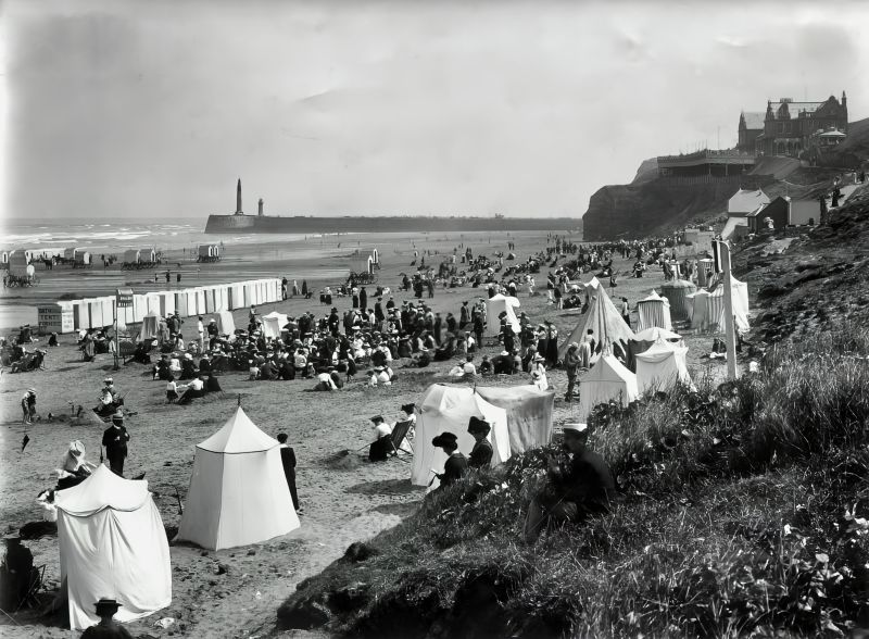 In the picture are bathing tents and bathing huts for hire during Edwardian times at Whitby Beach. The photo taken by the professional local photographer Tom Watson (1863-1957) also shows the considerable effort required to move the bathing huts backwards and forwards with the assistance of horses, in order to keep pace with the ebb and flow of the tide. Photographs like this one – taken by professional or amateur photographers alike – often show women’s large hats, white blouses, belted waists, simple long skirts and white parasols, which were the typical seaside fashion at the time. (Courtesy: Whitby Museum, Photographic Collection, LIB 487). 