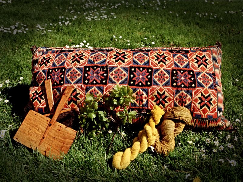 At weddings and other important festive occasions, brightly coloured seat and carriage cushions were used to sit on. These were backed, and the inside was padded. Like many other skilfully woven textiles in a home environment, the colours are surprisingly well preserved because these treasured textiles were kept in chests and cupboards for most of the years. | In the picture, wool yarn dyed in two yellow shades with oak leaves and 19th-century wool hand carders. (Private ownership). Photo: The IK Foundation.
