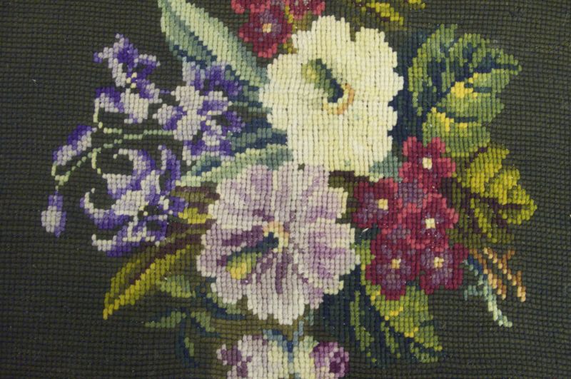Closeup detail of a Berlin wool work with a colourful flower motif against a dark green background in cross-stitch, circa the 1860s-1880s. Notice the strong-coloured purple, greens and mauve which indicate synthetically dyed shades. (Collection: Whitby Museum, Costume Collection, EMB4). Photo: Viveka Hansen, The IK Foundation.