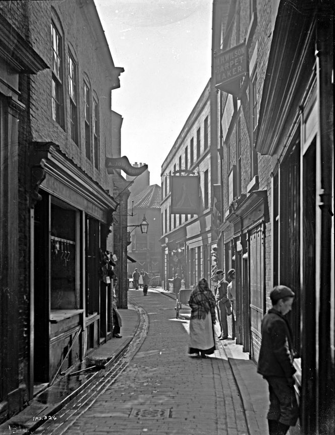 Many textile-related businesses were situated in close-by streets, gates and lanes of the old town, here depicted on photograph by Frank Meadow Sutcliffe taken in Sandgate circa 1880s-1890s. Also giving evidence for via repeated censuses, that many apprentices within drapery, tailoring and dressmaking were actively working as well as living in this area. (Courtesy: Whitby Museum, Photographic Collection, Sutcliffe 13-41D).