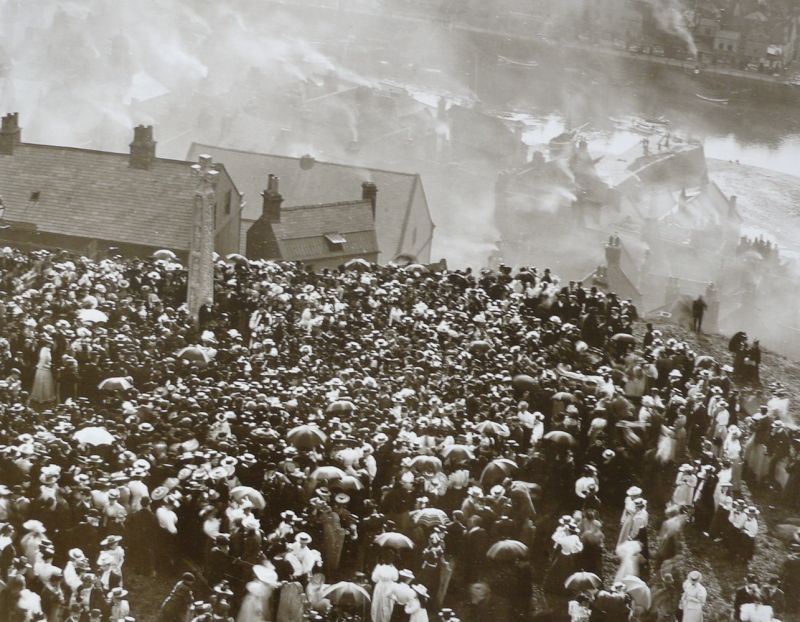 This photograph taken by Frank Meadow Sutcliffe from the church tower of Whitby Parish church, gives a rare opportunity to catch a glimpse of the use of umbrellas on a drizzling and smoggy day. The occasion can be dated exactly to 21st September 1898 when the Caedmon Cross was unveiled. (Photo: Frank Meadow Sutcliffe).