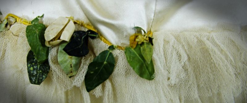 Only two of the ample Whitby Museum collections of white wedding dresses preserved date to before 1914: one from the early 1880s and the other from the Edwardian era. This is a close-up detail of the first-mentioned – an impressive late Victorian dress in cream-coloured satin with its long train would have needed a bustle to achieve its intended form. The bodice is decorated with flowers and leaves in silk or waxed-painted cotton, and is fastened to a white net. The upper part is boned as was fashionable at the time and lined with cream-white silk, with buttons covered in the same material as the dress. A little hat with ribbon and matching fabric flowers completes this expensive garment. (Collection: Whitby Museum…, Costume Collection, COS4.1). Photo: Viveka Hansen, The IK Foundation.
