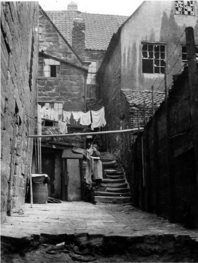 It is not possible to be sure whether this woman in Argument’s Yard in Whitby was washing for her family or was a professional laundress, but all the censuses list many women in Church Street and its yards who worked in the laundry business. Clothes and linen were often put out to dry in backyards. Research of the Poor Law valuation and continuous census returns during the 19th century also reveals that mangle houses were located along Church Street or the nearby yards. (Courtesy: Whitby Museum, Library & Archive, Photograph Book Four, 4/15).