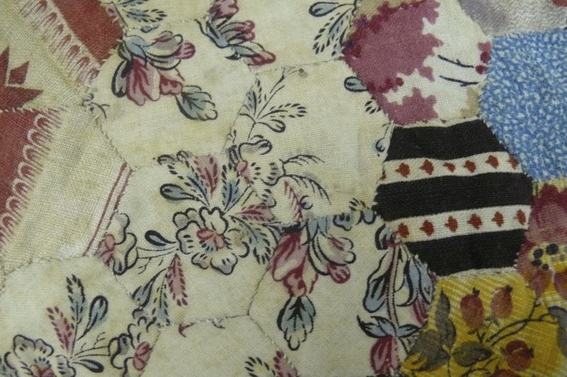 A patchwork quilt intended for a child’s bed, with small hexagonal patches sewn on by hand with white thread. These patches are arranged into what was commonly described as ‘Grandmother’s Flower Garden’. This little coverlet edged with a border measures 117cm by 138cm. Notwithstanding all the work that clearly went into it, the quilt was never completely finished, and one can still see tacking stitches along the edges and the padding and backing was never added. Moreover, the patchwork illustrated has been sewn with unusually small hexagons only an inch (2.54 cm) wide in printed cotton of every conceivable colour, but with blue and mauve dominant. The particular strong shade of mauve used proves that the fabric must date from after 1856, when aniline first made this shade of dye common. Mauve was never more popular than in the 1860s, so this patchwork probably mostly consists of left-over clothes/fabrics from that period, and itself was probably put together in the 1870s or 1880s (Collection: Whitby Museum, Costume Collection, GBB 125). Photo: Viveka Hansen, The IK Foundation.