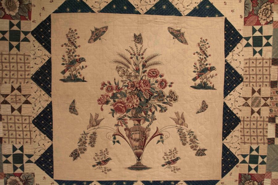 This second chosen quilt from the American Folk Art Museum, dating c. 1790s to 1810s also has an interesting  story to tell. As with many folk art objects its origin/artist is unknown or uncertain, while the center block  illustrated here on the other hand was printed by John Hewson (1744-1821). He was a British calico printer  moving to America in 1774 – with the help of a letter of recommendation from Benjamin Franklin – establishing  his business in an area outside Philadelphia where he advertised for “printing calicoes and linens for gowns,  &c., coverlids, handkerchiefs…” Hewson was a skilled worker and just such an artisan tradesman that was  seen as important for the needs of the people in the American colonies. There are other examples as well in  American collections of bedcovers including Hewson’s block printed vase overflowing with flower motifs, such as  in the extensive collection of Philadelphia Museum of Art [Blum, Dilys E., The Fine Art of Textiles…p.93]  (American Folk Art Museum, New York, no 2006.5.1). Photo: The IK Foundation, London.