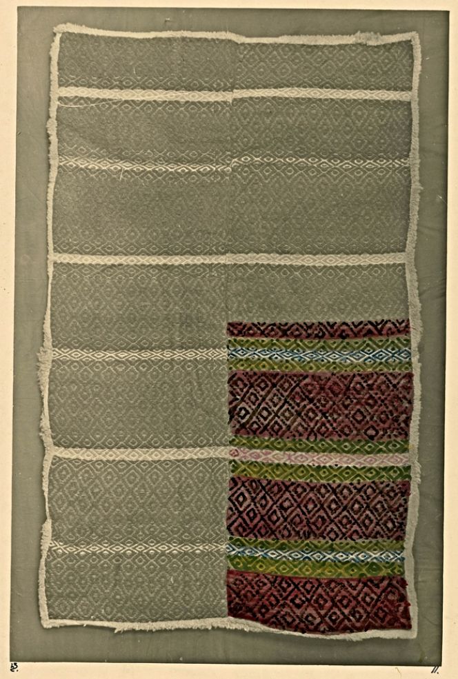 This handwoven bedcover, with the upper side in the techniques “gåsögon” and rose path, whilst the back is lined with a sheep felt for warmth, was photographed and partly coloured in the early 20th century. It was part of an almost monumental inventory of the country people’s textiles in Sweden, compiled by Lilli Zickerman (1858-1949) during 1910-1932. Today, the originals are kept at the Nordic Museum in Stockholm, comprising approximately 24,000 written records, sketches, and black-and-white photographs, including many partly hand-coloured pictures, such as this illustrated bedcover. The geometric design measures 138 cm × 205 cm and was woven on a linen warp with a wool-and-cow-hair weft, at an unknown date. This multicoloured textile is evidence that the “gåsögon” technique’s distinctive geometric design was popular on a variety of household textiles. On the coarsest of bedclothes, but also fine linen tablecloths during the 19th century.|Sunnerbo district, Småland province, Sweden. (Courtesy: Hemslöjdens Samlingar, Zickermans studiesamling. HSZ.80-07528. DigitaltMuseum). 