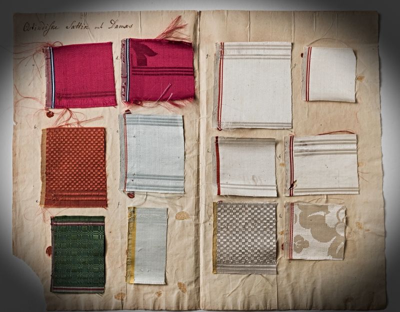 This selection of fabrics – named ’East Indian Satin and Damask’ – most likely originated from the Swedish East India Company imports, included in Anders Berch’s educational collection, circa 1736 to 1774, according to his years of work. For instance, the sample marked (a) was described as follows in the research by The  Nordic Museum et al. (Stavenow-Hidemark, Elisabet, ed. 1991, p. 184). ‘Damask of 5-end satin. The motif is in weft effect against a background in warp effect. Selvage of basket weave and satin. Bands of different structure (end of piece)’.  It is noticeable that damasks and satin samples are similar in colours and designs to silk qualities carried on the ship ‘Götha Leijon’ in 1752. (Courtesy: The Nordic Museum.… NM.0017648b:11. DigitaltMuseum).