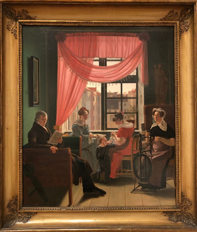 Portrait of a bourgeoise Copenhagen family in 1828, painted by the Danish artist Emilius Bærentzen (1799-1868), who had been one of Christoffer Wilhelm Eckersberg’s students – the master painter discussed above – at the Danish Academy in the early 1820s. Noticeable in this tranquil and melancholy home interior depiction is that it demonstrates traditional family values in the form of various ongoing female handicraft, a young son playing calmly in his paper tricorn hat and a father who reads a newspaper. Especially informative details of textile work, visualise that the mother (or maybe a daughter) wears an apron for protection of her black silk or cotton dress when spinning wool on the spinning-wheel. Whilst, two daughters are seated close to the open window to get the best possible daylight for sewing and knitting. The curtain arrangement – draped and tied back to one side – gives a pleasant light for the room and further gives an impression of the peaceful everyday atmosphere of the apartment. (Collection: Statens Museum for Kunst, København, Denmark. No: KMS8588. On display in 2021). Photo: Viveka Hansen, The IK Foundation.