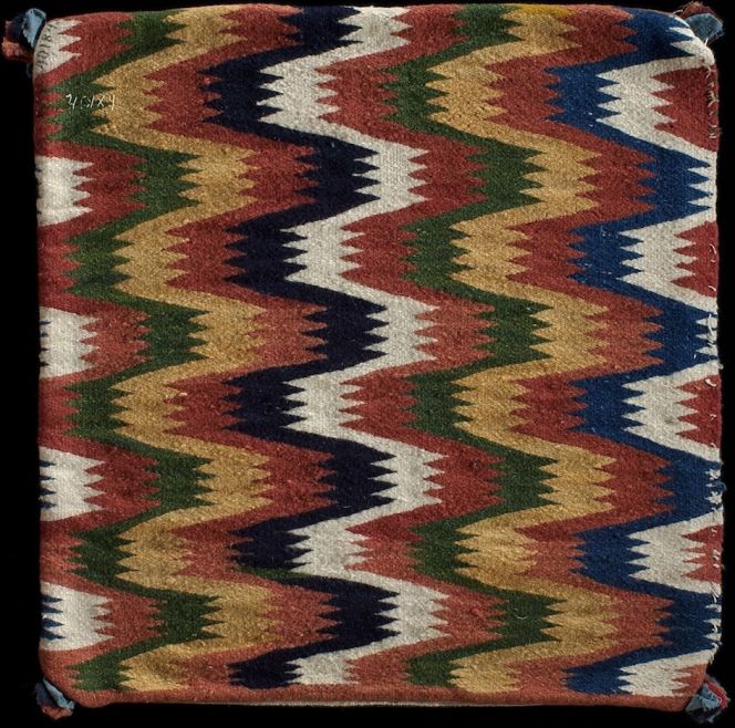 Well-preserved early 19th century square-shaped cushion in perfectly symmetrically woven zigzag motifs. Handwoven in the double interlocked tapestry technique on a linen warp and woollen weft. Pieces of wadmal cloth strengthened and decorated the corners, whilst traces of down remains within the cushion. Woven in Östra Göinge district, Skåne province, Sweden. (Courtesy of: Nordic Museum, Stockholm. NM.0040184, front. Digitalt Museum).