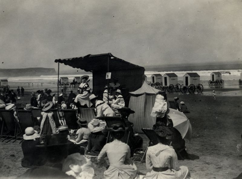 This view of a summer day on the beach on the west side of Whitby illustrates what seem to be mainly summer tourists in light-coloured clothes listening to musical entertainment. Even the woman musician and the two men glimpsed on the stage are dressed entirely in white. To enjoy a day on the shore as a bystander dressed in a delicate white cotton dress was mainly possible for the well-off and middle classes, judging by this and other similar photographs from circa 1905. Even more extensive groups of society could enjoy a summer Sunday at the beach in late Victorian and Edwardian times than in earlier years. (Courtesy: Whitby Museum…, Photographic Collection, C 525).