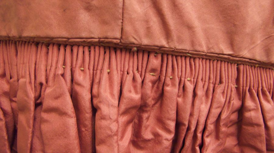 A dress from the Whitby Museum collection demonstrates how tight gatherings were prepared and sewn together with coarse linen thread in this hand-sewn silk dress, dating mid to late 1850s. In general, drawing together considerable width in tight pleats of this kind especially in the back half of the skirt had long been a custom in England as in other countries. This was an unsurpassed design detail when it was necessary to draw together a skirt 3 or 4 metres in circumference in the smartest possible way. Red silk fabric dress c. 1855-60. (Owner: Whitby Museum, Costume Collection, GBD 13). Photo: Viveka Hansen.