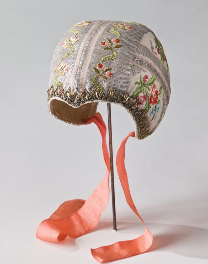  This well-preserved cap was part of the Christening costume for Märta Helena Reenstierna’s and Christian Henrik von Schnell’s children being born between 1776 and 1787. This small garment just as the second cap below, must have been very sentimental objects for Märta Helena and her husband as seven of the eight children died when young. Probably being kept in a chest or drawer, for best safekeeping. Judging by the diary introduced first in 1793, such a delicate garment seems not to have been made by the young mother herself, but instead by several craft skilled individuals. Maybe she choose the fabric etc, assisted by a seamstress who stitched the fine cap of silk brocade with a cotton lining and attached red silk ribbons. The gold metallic bobbin lace was probably of French origin and purchased from a shop in Stockholm. This assumption is strengthened by that the rigorous sumptuary laws from 1766 was revoked by Gustav III during his reign from 1772 to 1792 – a period when all sorts of imported luxury goods became immensely popular in the well-to-do strata of society. (Courtesy of: The Nordic Museum. No: NM.0000638). 