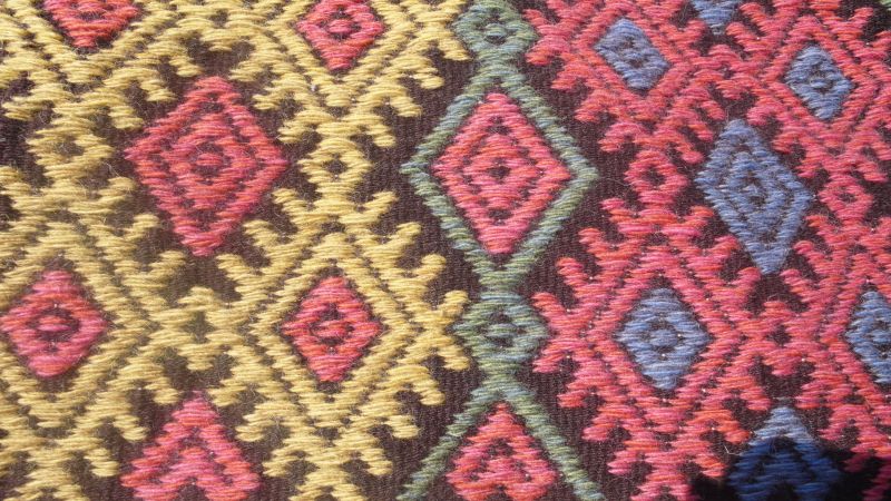 Close-up from the reproduction demonstrating how the colours for the ornamentation – here red, yellow, green and blue – were used simultaneously on the dark brown main weft-faced tabby. Photo and woven fabric: Viveka Hansen.