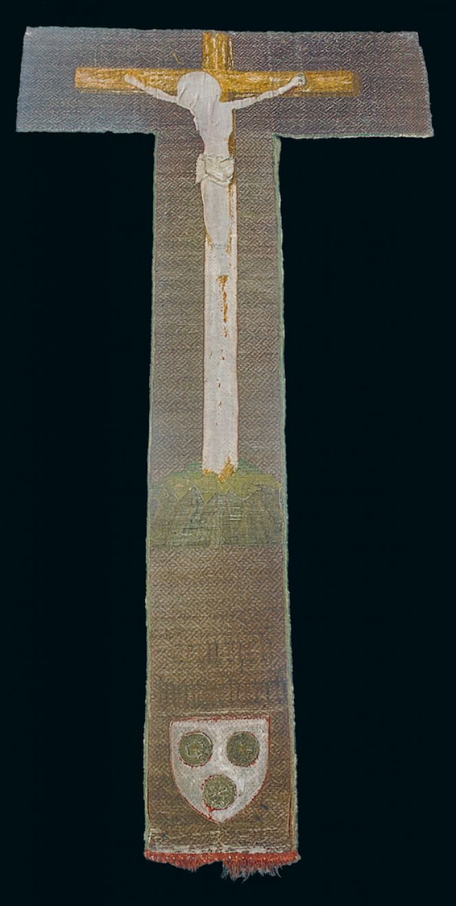 A preserved cross with a partly fragmented crucifix dating from the  second half of the 15th century, which originally decorated a chasuble  in St Petri church. The image of Christ was made of a creme-white silk  fabric in an appliqué technique, at a close study it is also possible to  see stitching in grey for the nail and red from the wound on the right  hand. Even the “plaiting motif” of the fabric surface was  embroidered with a very fine golden thread assisted by red stitching  of silk in so-called laid work. This complex piece is believed to have  been made by a professional embroiderer on the Continent. The donor’s  name of this vestment – Heinrich Dringenberg – was stitched in Gothic  lettering and his coat of arms with three golden roses was inserted on an  originally red ground. This part of the work could have been added by the  same embroiderer. Height 104 cm & width 16 cm. Photo: The IK Foundation, London.