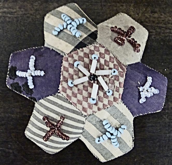 When doing patchwork one preferably need templates made from some strong, durable material that would enable, for example, to cut out hundreds of paper hexagons identical in size and shape as models for pieces of cloth. The Whitby Museum Social History collection contains a rhombus shaped zinc template, together with the beginnings of two pieces of patchwork and two patchwork pin-cushions. The simpler of these pin-cushions has been made from pentagons of various colours sewn together, while the other – illustrated here – was made up from seven hexagons with each of the sections further decorated with a collection of small beads. Objects dated to around the 1880s to the 1910s. (Collection: Whitby Museum, Social History Collection, unnumbered at time of research.) Photo: Viveka Hansen, The IK Foundation.