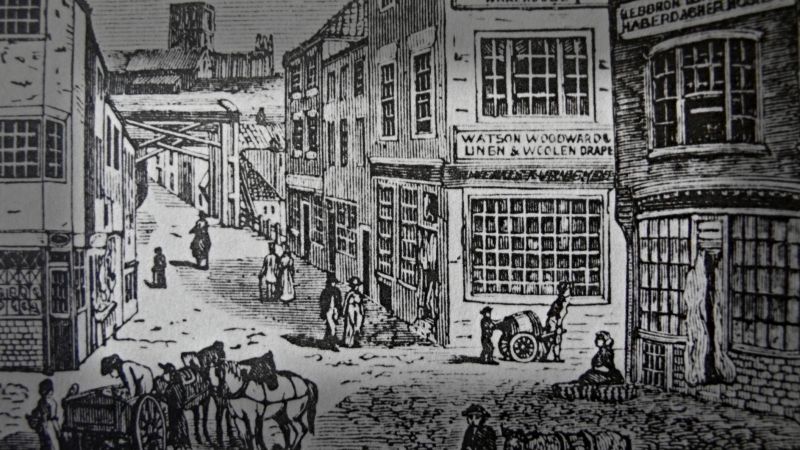 The thorough historical studies by the two local antiquarians also give information on other textile activities during the period from 1779 to 1840, together with more sporadic observations of visitors. Young’s 1817 book on Whitby for example, reveals an interesting fact about the tradesmen and manufacturers of the day, mentioning 30 drapers. He even suggests that there might be too many of them: ‘Their number is at present too great for all to prosper’, which can also be understood from the fact that the town contained 69 ‘tailors, including staymakers’. Other tradesmen with textile connections were ‘5 cabinetmakers and upholsterers’ and ‘6 slop-shops’ – shops which sold inexpensive or good-value second-hand clothes. | Close-up detail of a contemporary image, which shows the Haberdashery shop etc at the Old Market Place in Whitby 1818. (Collection: Whitby Museum, Library & Archive, Dr. English Prints). Photo: Viveka Hansen, The IK Foundation.