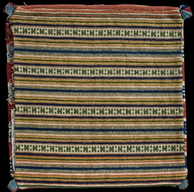 The back of the same cushion, demonstrates the same perfection by the weaver. As customary the back was outlined in a “simpler” style however, here in a weft ribbed technique. This way of designing a cushion, meant that the shuttle could be in constant use making it quicker to weave, contrary to the complex zigzag front which was made like a tapestry when the weaver manually had to interlace each woollen colour to its designated area. (Courtesy of: Nordic Museum, Stockholm. NM.0040184, back. Digitalt Museum).