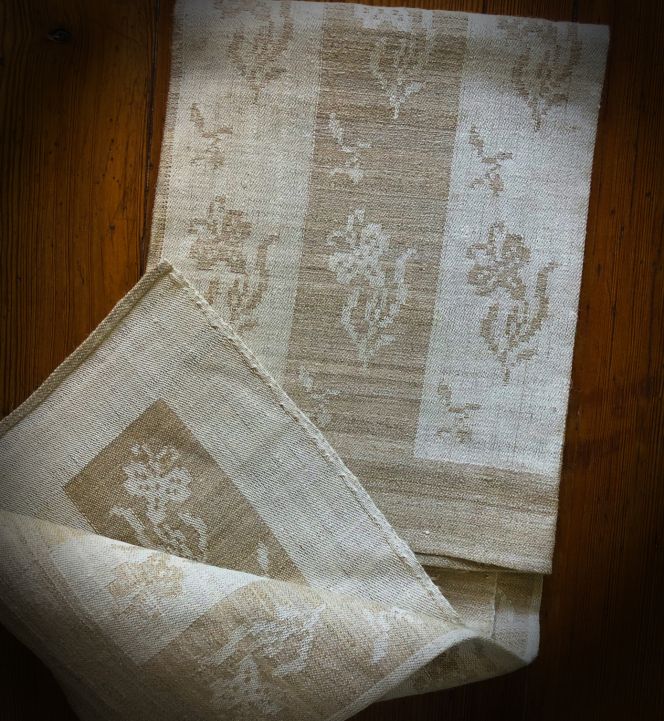 This linen damask towel, featuring repeated carnation motifs, was acquired from Malmöhusläns Hemslöjdsförening (the Handicraft Organisation of Malmö County) during the 1950s or 1960s. The professionally handmade towel, measuring 49 cm by 69 cm, was woven by one of the organisation’s female damask weavers on a loom equipped with a shaft draw system. The very delicate warp consisted of a 1-ply bleached and unbleached linen (approximately 24 threads per centimetre), while the weft was spun from a hand-spun linen thread (around 26 threads per centimetre). The use of hand-spun linen for the weft and the hand hemming further emphasised the high quality of this household textile. The towel came into my ownership through inheritance. Due to its exceptional fineness, it has never been used and has always been regarded as a “museum piece”. (Private ownership). Photo: Viveka Hansen, The IK Foundation.