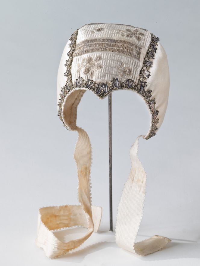 This somewhat plainer Christening cap in just as good a condition, is the second such baby garment used in the Reenstierna family during the 1770s and 1780s. One may speculate if this one was intended for the boys and the more colourful one above for the girls! However, the design being similar and lined with a fine cotton quality, but a silk brocade was chosen for the top part only, whilst a plain white silk fabric was used for the side parts of the cap. The exquisite silver metallic bobbin lace being the main feature together with white silk ribbons to tie under the cheek. (Courtesy of: The Nordic Museum. No: NM.0000639).