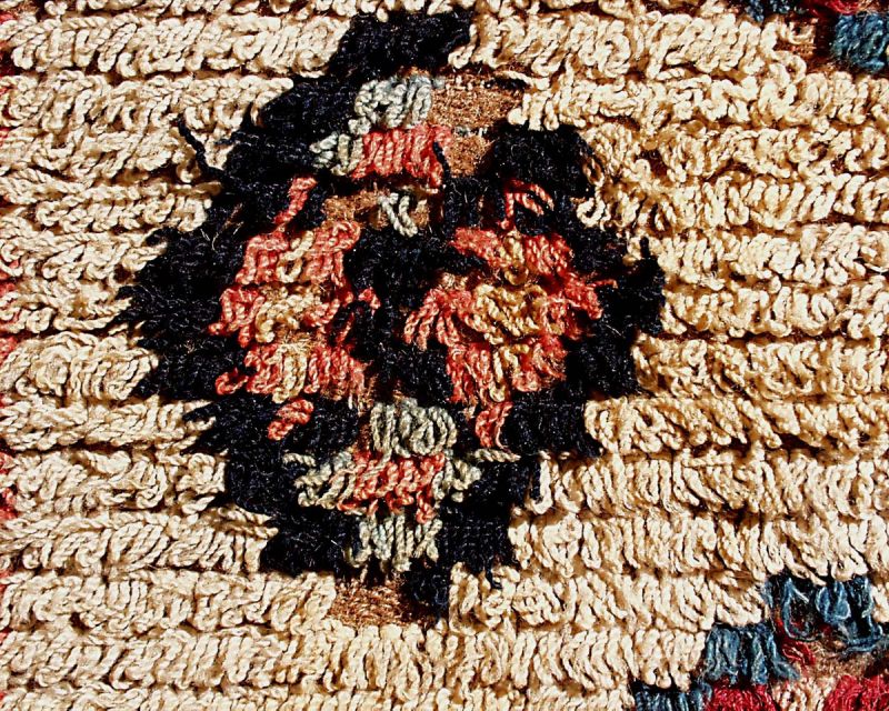 Fully-piled “rya”, woven and used for a warming bedcover in the province of Bohuslän, Inland Torpe district. This detail gives a close-up view of the technique, illustrating that in this area the woollen knots formed an uncut loop piled surface and its colourful geometrical motifs were exactly positioned on the white ground. The bedcover, finished off with a wide border of geometrical star designs was woven in a half-width in a traditional narrow handloom, which made it necessary for the weaver to make two almost identical woven pieces and after the weaving these were stitched together to make a full-sized bedcover. (Courtesy of: The Nordic Museum, NM.0095884, detail).