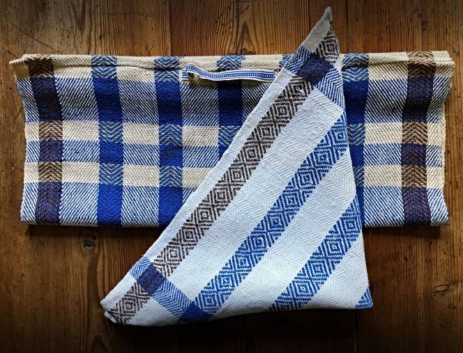 A second attempt at the technique used two towels, with a cotton warp and a linen weft. This is a variation of the technique “gåsögon,” with the threading arranged in different groups to produce a striped effect in this twill variant. The visible difference between the two depicted towels was achieved by the shedding order and the chosen colour of the linen weft thread. The towel at the back was woven in chevron twill; that is, the shedding order was repeated as 1, 2, 3, 4, and a light brown weft thread was used. Whilst in the towel at the front, woven on the same warp, white linen yarn was used for the weft, and the shedding order was turning at regular intervals (1, 2, 3, 4, 1, 2, 3, 4, 3, 2, 1, 4, 3, 2, 1 and so on) to get the diamond-shaped “gåsögon” design. (Private ownership). Photo and woven towels: Viveka Hansen, The IK Foundation.