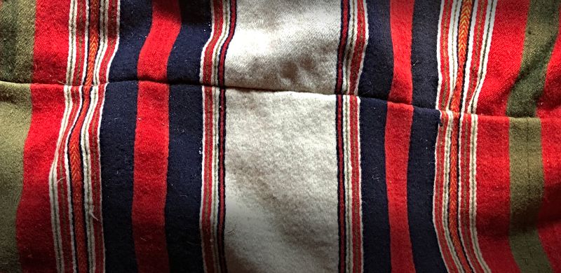 To be compared with the bed textile in the painting above, this well-preserved striped feather bolster was woven in a very densely beaten twill, and as customary after the weaving, due to the limited handloom width, two identically woven lengths of fabric had to be stitched together to get the required width. Furthermore, this particular warming feather bolster is part of the so-called Onsjöstugan [cottage from Onsjö], initially located in the central part of Skåne province, but for many years back at the open-air museum Kulturen. The museum aims to show how such a cottage used to be furnished around the year 1850, among other sources, with similar furniture and household objects as were stated in estate inventories after Sven Andersson and his wife, Gunilla Andersdotter, dated 1842 respectively 1865, who lived in this cottage. (Collection: Kulturen in Lund, Sweden). Photo: Viveka Hansen, The IK Foundation.