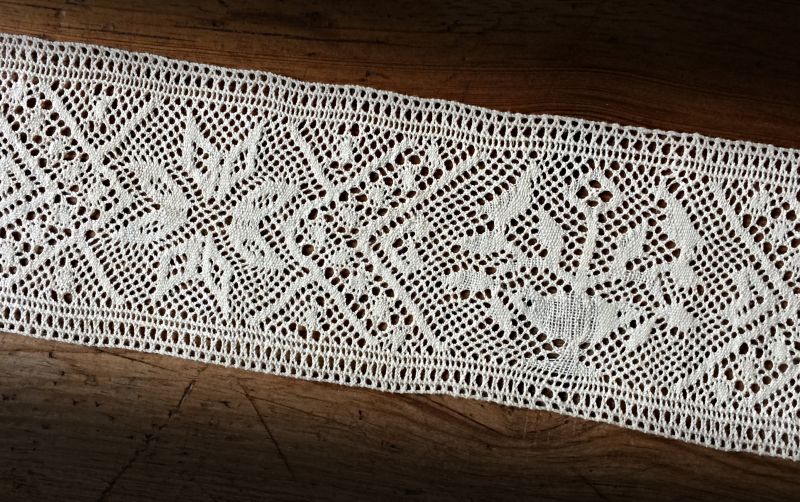 This traditional handmade linen bobbin lace from the province of Skåne was made in an unknown year during the 19th century. This is an advanced lace with a width of 6 cm, depicting stars and opposite-standing birds in a tree of life. All these motifs were popular for other contemporary handcrafted home furnishing textiles too from the region, like tapestry weaving, art woven cushions of several techniques, whitework embroidery, etc. 48 pairs of bobbins were used in this complex and beautiful lace. (Private ownership. Photo: Viveka Hansen).