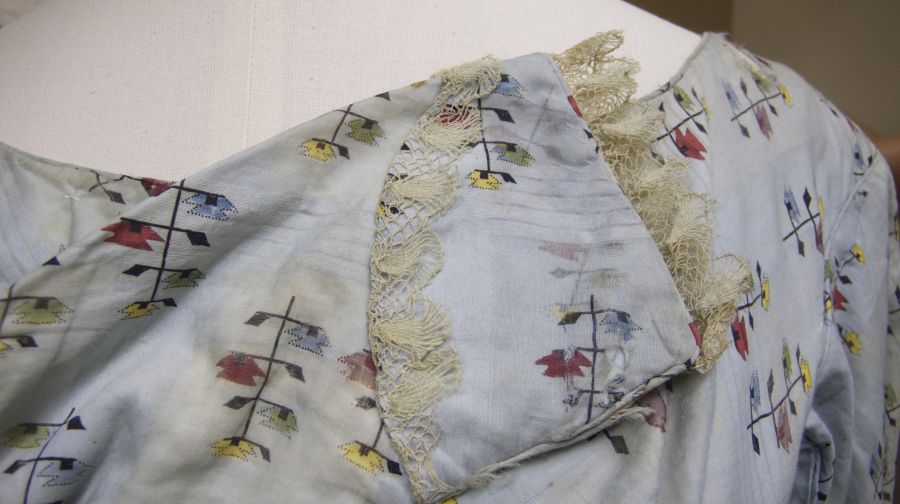 Close up study of a dress, circa 1820. Printed cotton and handmade bobbin laces. In the period from 1810 to 1825: Cotton day dress with waist high under the breast – the waist line began to drop at the end of this period – long narrow sleeves with puffed or narrow shoulders in printed cotton with a small motifs, flounce on the edge of the skirt; a straight style with many similarities to the previous fifteen years. White muslin cap preferably with bobbin lace and openwork embroidery, tied under the chin. (Dress: Whitby Museum, Costume Collection, unnumbered at time of research). Photo: Viveka Hansen.