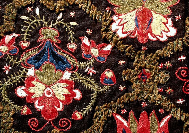 A close-up detail of a partly piled weave, where the surrounding greenish lattice-work was the only piled knots, together with geometrical star motifs in a voided pile weave border (not depicted). Whilst, the colourful finely shaped woollen embroidery represents the focal point on this carriage seat cushion, marked with ‘ANO 1835’ and the initials ‘ECD’ ‘OAS’ – woven and embroidered by the same woman who had both craft skills or by two separate women in Wemmenhög district, Skåne province in southernmost Sweden. Even if not evident, it appears to have been made for a young bride’s dowry, due to the initials of one female name (ending on D = dotter [daughter]) and one male name (ending on S = son [son]). (Courtesy of: The Nordic Museum, NM.0018439, detail). 