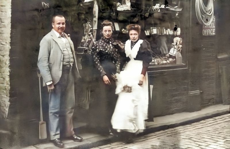 A third photograph also demonstrates that some women favoured coloured shirts with printed motifs in a fashionable style or, by regulations, a black shirt as part of a working uniform. Here exemplified with two young ladies together with a small child and, probably, the shop’s owner outside a general dealer selling baskets, porcelain, etc., in Baxtergate, Whitby, photograph about 1902. Garments of this kind may well have been made locally at Remmer’s Shirt Factory. (Whitby Museum, Photographic Collection, W 4335. Whitby Lit. & Phil. Modern digital colouring of the old picture).